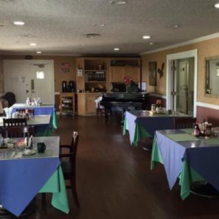 An empty restaurant dining area with tables set and covered in blue and green tablecloths.