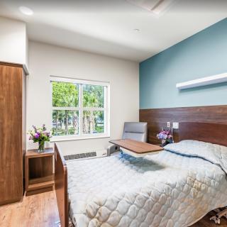 A minimalist hospital room with a single bed, wooden furniture, and a window view.