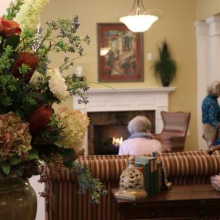 A cozy living room with a flower arrangement and people relaxing near the fireplace.