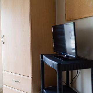 A small television on a black stand next to a wooden wardrobe in a room.