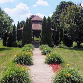 A picturesque garden pathway leading to a charming house, surrounded by neatly trimmed trees and colorful flower beds.
