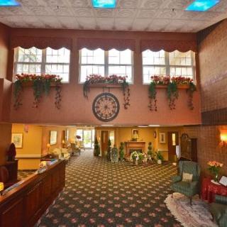 A warmly decorated hotel lobby with a reception desk, patterned carpet, and large clock on the wall.