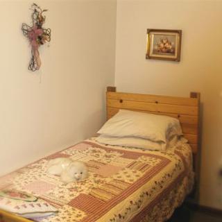 A simple bedroom with a single bed featuring a quilt and pillow, adorned with wall art and a cross decoration.