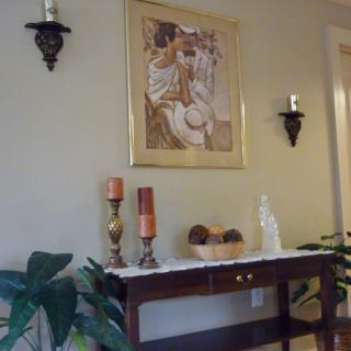 An elegant interior setting with a decorative table topped with candles and plants beneath a framed painting.