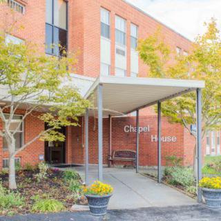 A brick building entrance with a canopy and surrounding greenery.