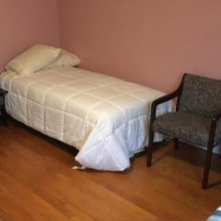 A simple bedroom with a single bed, chair, and nightstand.