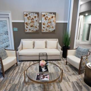 A modern living room with a sofa, two chairs, and a glass coffee table, accented by decorative pillows and wall art.