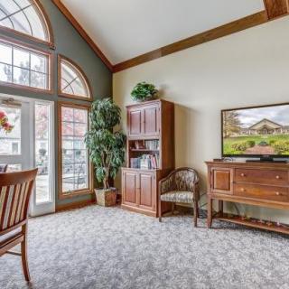 A cozy living room with a large window, wooden furniture, and a TV.