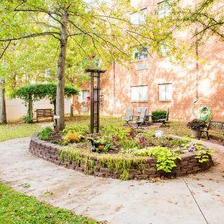 A well-maintained garden area with trees and plants, adjacent to a brick building.