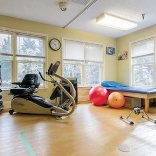 A well-lit therapy room with exercise equipment, including a stationary bike and colorful exercise balls.