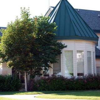 A residential house with a green conical roof and large windows, surrounded by trees and landscaping.
