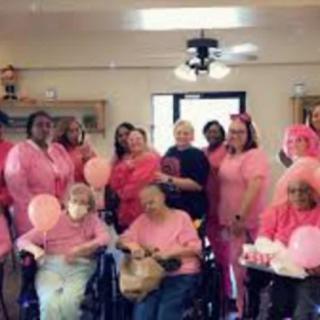 A group of people gathered indoors wearing pink clothing, celebrating with balloons.