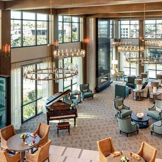 A spacious and elegantly designed lobby featuring multiple seating areas, a grand piano, large windows, and chandeliers.