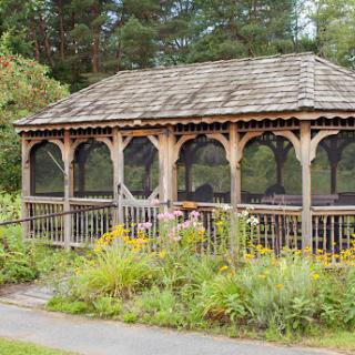 A charming wooden gazebo surrounded by vibrant flowers and lush greenery.