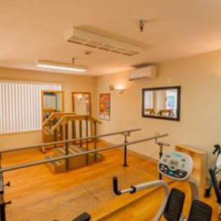 A rehabilitation room equipped with exercise equipment, featuring handrails and mirrors for physical therapy.