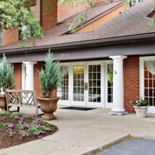 A welcoming building entrance with brick facade and white columns, surrounded by potted plants.