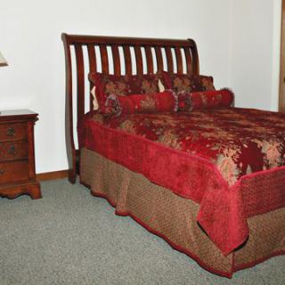 A cozy bedroom with a bed featuring red bedding and a wooden nightstand with a lamp.