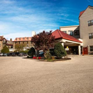 A view of a hotel entrance with a landscaped driveway under a clear blue sky.