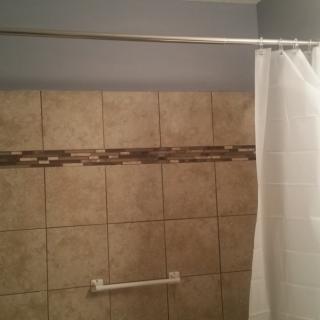 A bathroom with a tiled wall and a shower curtain hanging from a rod.