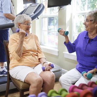 Two elderly women exercising with hand weights in a fitness room.