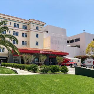 A view of a hospital building with a red awning and lush green lawn.