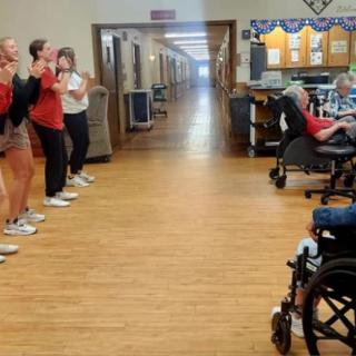 Cheerleaders performing for seniors in a nursing home hallway.