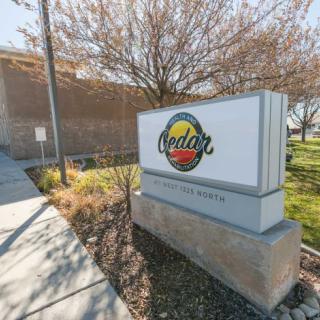 Image of an outdoor company sign with a logo next to a building and a sidewalk.