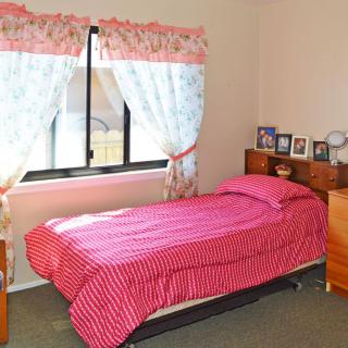 A cozy bedroom with a single bed dressed in pink bedding, complemented by floral curtains and a small wooden nightstand.