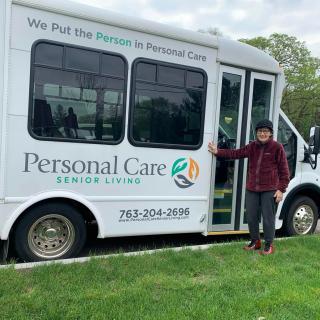 An elderly person standing next to a Personal Care Service Living bus.