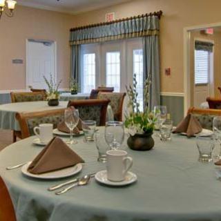 A well-arranged dining room with neatly set tables, featuring place settings and decorative plants.