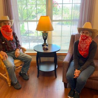 Two people dressed in cowboy attire, sitting indoors with hats and bandanas.