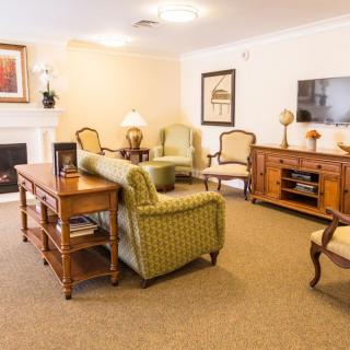 A cozy living room with classic furniture, including a sofa and armchairs around a coffee table, a fireplace, and a TV stand.