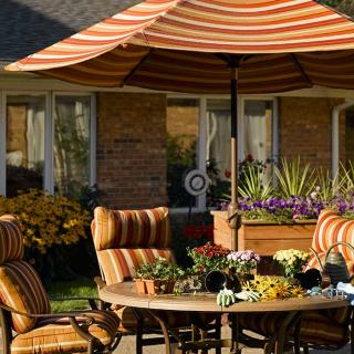 A cozy patio with striped furniture and a large umbrella, surrounded by a lush garden.