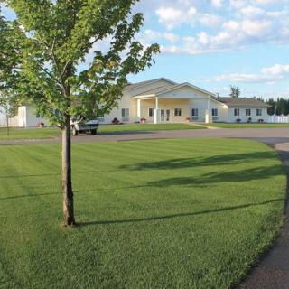 A building surrounded by a well-maintained lawn and clear blue skies with scattered clouds.