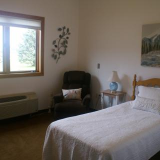A simple bedroom with a single bed, window, chair, and lamp.