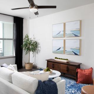 A modern living room with a white sofa, coffee table, and wooden furniture, featuring wall art and a potted plant for decor.