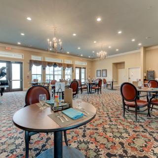 A spacious and elegantly decorated dining room with several tables and chairs, adorned with chandeliers and a patterned carpet.