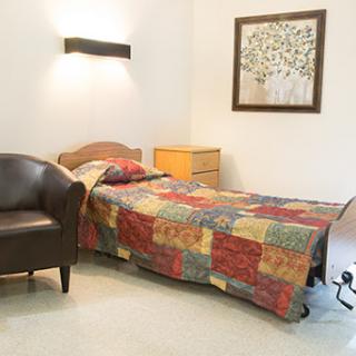 A cozy bedroom featuring a patchwork quilt on the bed, a comfortable chair, and decorative wall art.
