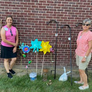 Two individuals pose beside colorful garden decorations in an outdoor setting.
