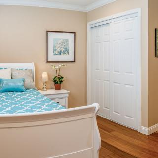 A cozy bedroom featuring a bed with a blue patterned cover, a nightstand with a lamp and plant, and a closed closet with sliding doors.