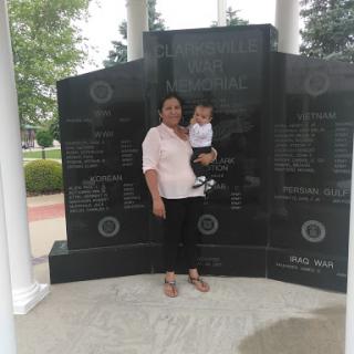 A woman holding a child stands in front of a memorial monument.