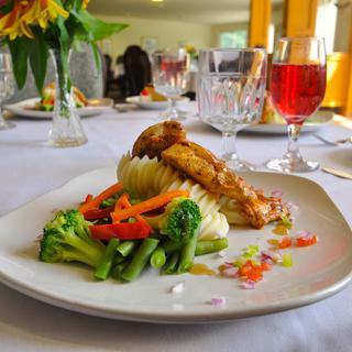 A beautifully plated gourmet meal featuring chicken and mixed vegetables, accompanied by a glass of wine on an elegantly set table.