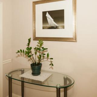 A glass table with a potted plant beneath a framed picture in a hallway.