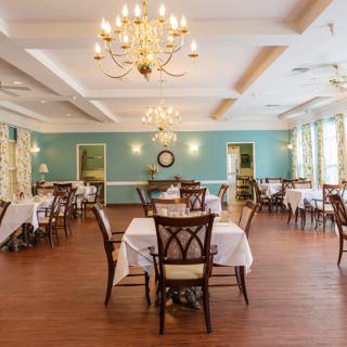 An elegant dining room with neatly arranged tables, chandeliers, and a wooden floor.