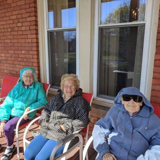 Three elderly women sitting on a porch, bundled up in coats, enjoying the outdoors.