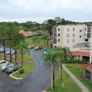 Aerial view of a hotel with parking area and palm trees.