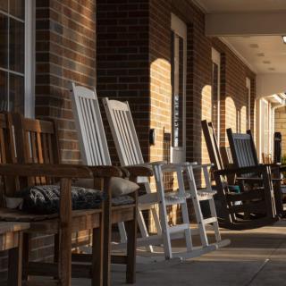 A row of rocking chairs on a porch, casting long shadows in the sunset.