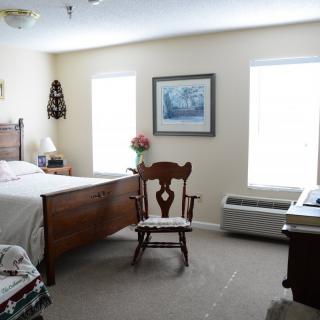 A cozy bedroom with a wooden bed, chair, and two windows bringing in natural light.