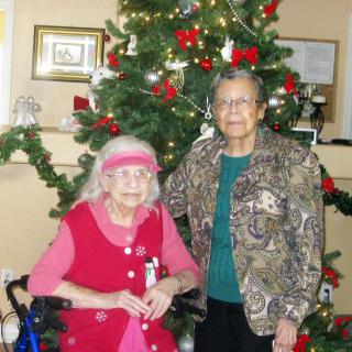 Two elderly women posing in front of a decorated Christmas tree.