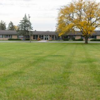 A building with a large grassy field and a tree in the foreground.